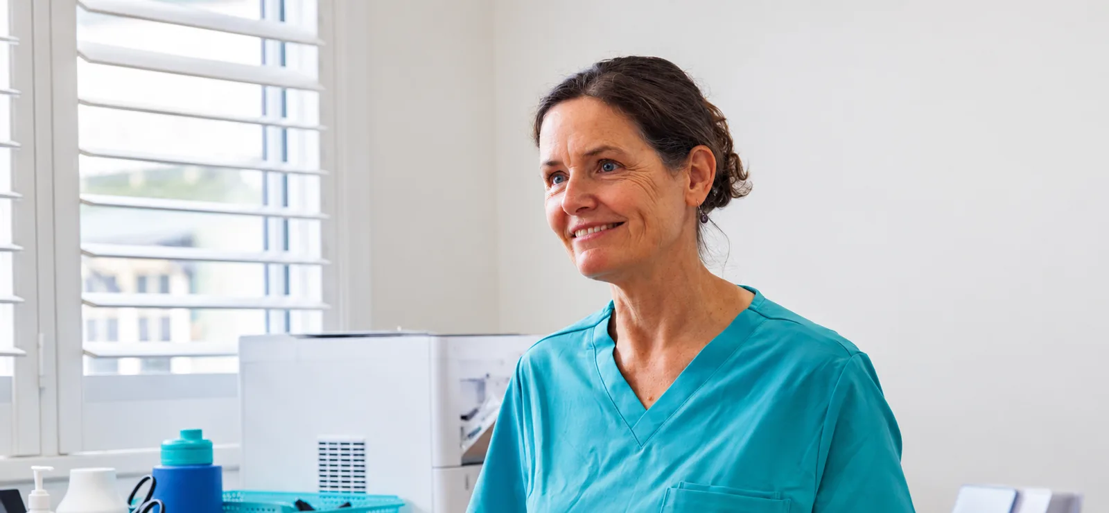 Doctor in teal scrubs smiling in a bright clinic room