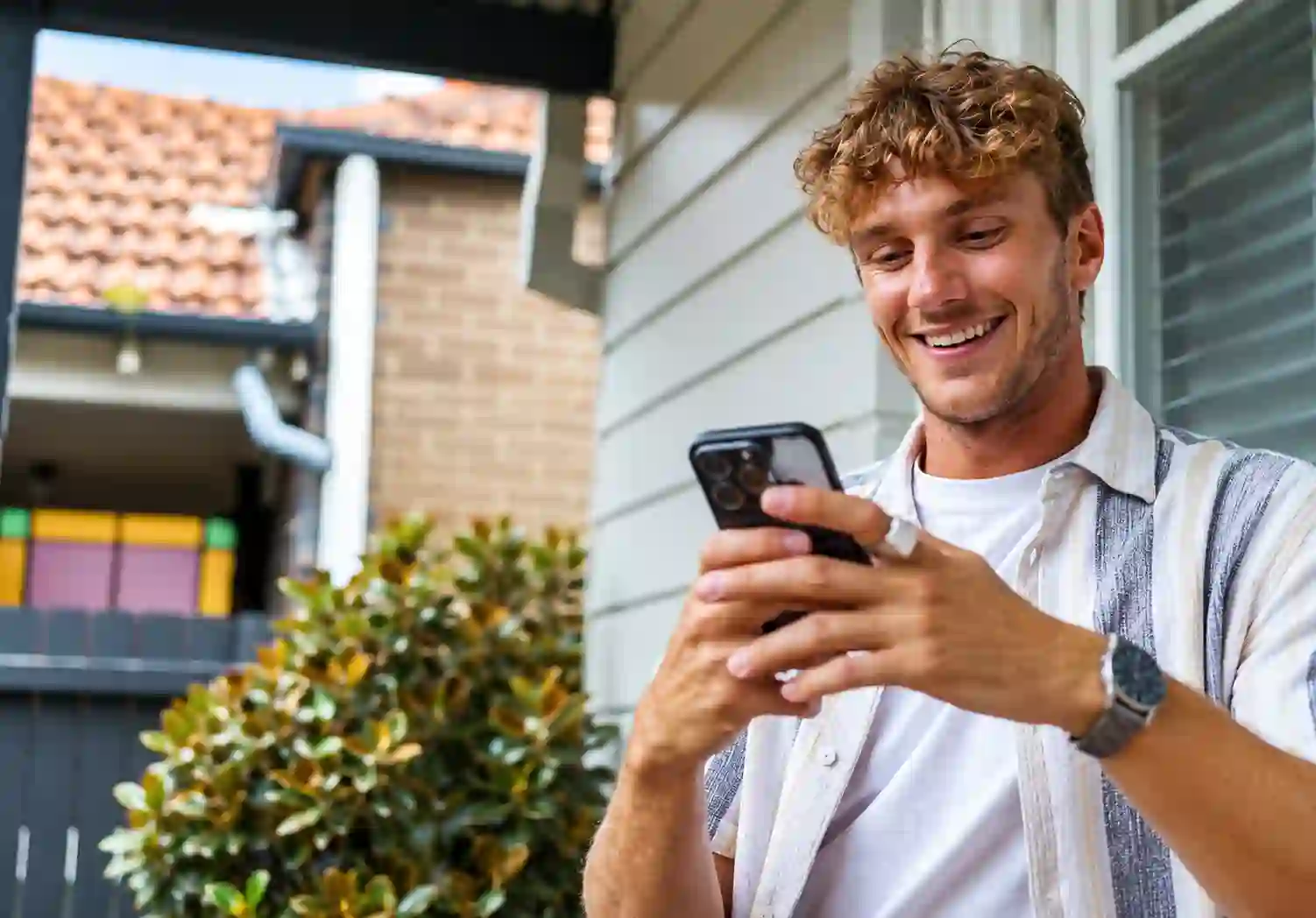 Man smiling at his phone outside his home